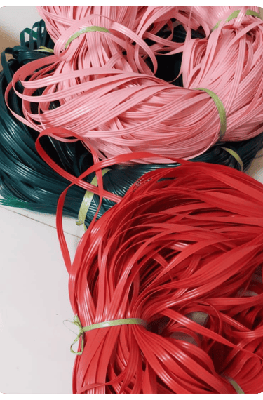 Colorful recycled plastic weaving strips in red, pink, and green prepared for handmade woven bag crafting at Craftvitas
