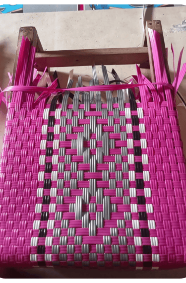 Early weaving process of a pink patterned handmade plastic woven bag at Craftvitas Indonesia.