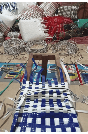 Shaping the base of a yellow and white handmade woven bag using recycled plastic weaving strips at Craftvitas Indonesia.