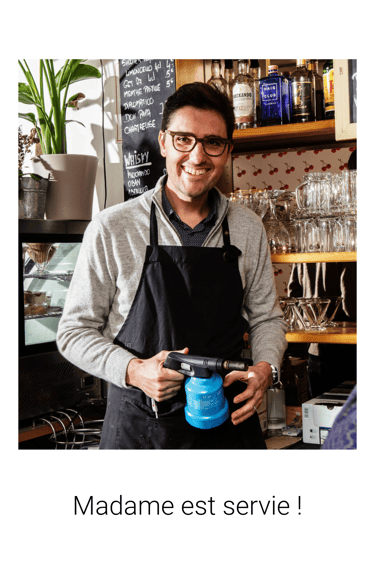a man in a black apron and glasses holding a blue mug