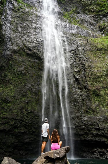 a couple of people standing in front of a waterfall in hawaii