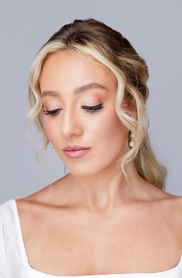 Bride with blonde hair styled softly back, soft glam wedding makeup, glowing skin, long lashes, and natural pink lipstick.