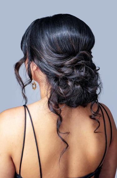 Woman with textured low bun updo and loose curls wearing black strappy dress, elegant hairstyle perfect for wedding or prom.