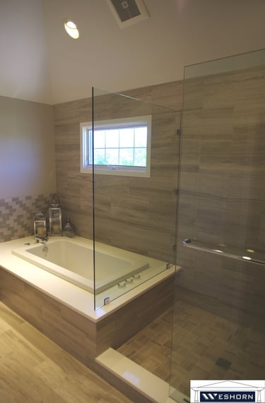 Modern master bathroom featuring a soaking tub next to a glass walk-in shower with neutral stone tile.