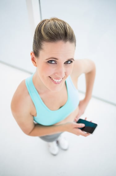 Smiling woman in blue fitness apparel holding a smartphone during her gym workout.
