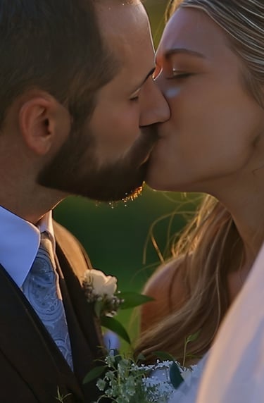 A bride and groom share a kiss at sunset on their wedding day, with the bride’s veil flowing in the