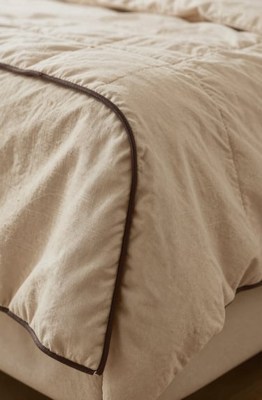 Detailed shot of the quilt's corner showing the hand-sewn binding in a dark espresso thread, contrasting elegantly with the soft sand fabric.
