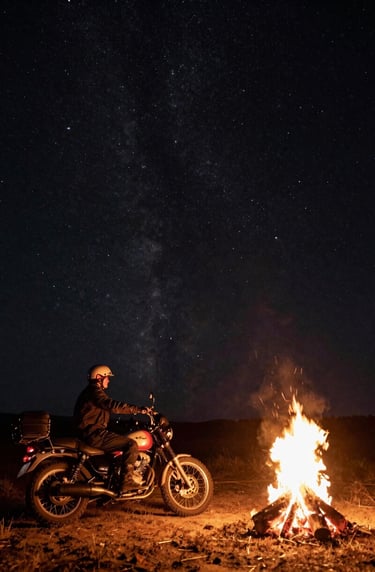 A wide, atmospheric shot of a lone rider and motorcycle parked by a small fire under a vast starlit sky in a Global / Western wilderness. The scene uses rich charcoal black for the night sky and warm soft off-white for the fire's glow.