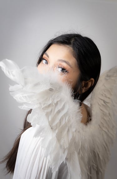 A self portrait, mostly white, over the shoulder peeking at camera through angel wings.