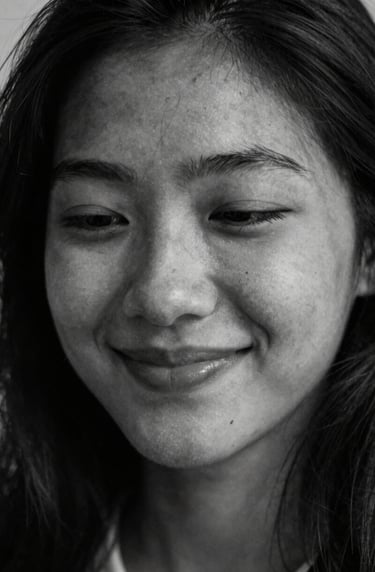 A candid, sensitive moment captured in black and white style but with deep dark charcoal and off-white tones. A soft smile partially hidden by shadows, evoking deep artistic appreciation.