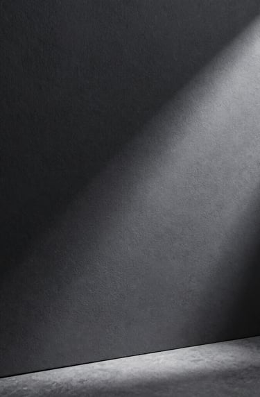 A clean, minimalist composition showing a single thin ray of light hitting a textured charcoal surface, elegant atmosphere, professional studio shot, European / Spanish style.