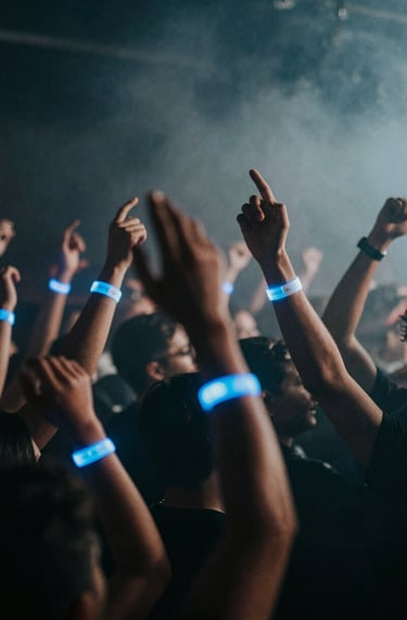Atmospheric shot of a dancing crowd with hands raised, glowing wristbands in #7A7CF1, hazy smoke, dark nightclub background #0A0A0F.