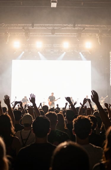 Wide-angle shot of a crowd at a professional music venue in a North American city. Silhouettes against bright off-white stage lights, capturing an immersive and emotionally powerful live concert experience.