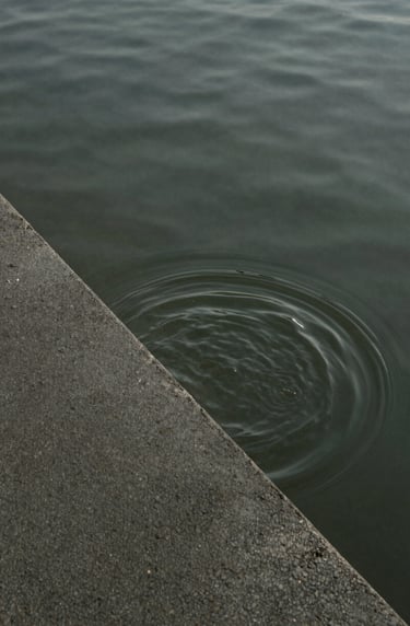 Minimalist abstract photo of water rippling over a textured concrete surface, symbolic of urban water systems, muted charcoal and olive green tones.