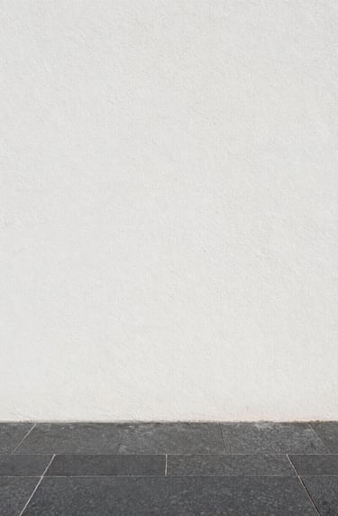 Vertical shot of a white stucco wall meeting a dark gray stone floor, minimal shadow line, editorial architectural detail, clean and sophisticated.