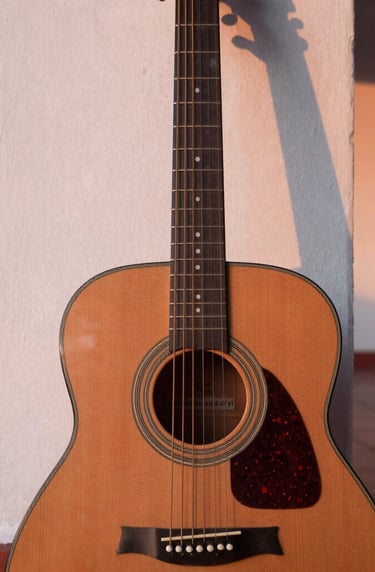 A high-quality close-up of an acoustic guitar leaning against a colonial style wall in a Venezuelan patio during sunset, soft rose and off-white light highlights on the strings.