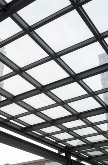 A low-angle shot of a glass and steel canopy in a US city. The framework creates a grid pattern of charcoal gray lines against the bright white light of the sky. The image reflects clean lines and sophisticated geometric precision.