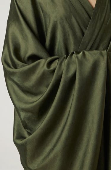 A detailed photograph of a silk sculpture's surface, showing the rich, meticulously layered texture. The color palette is a sophisticated blend of deep forest green and muted olive, with a clean and modern composition.