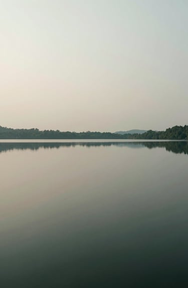 A high-contrast photography piece of a still lake reflecting a hazy sky, minimalist and captivating, featuring deep tones of #362C27 and soft #A89B90 highlights.