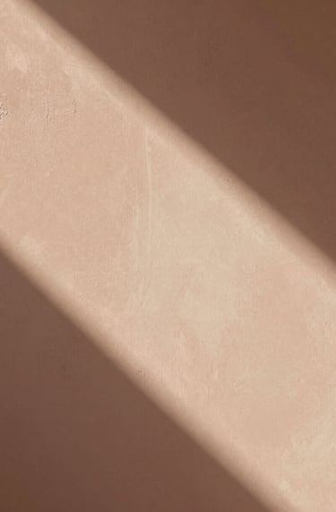 An abstract, artistic photograph of soft morning light hitting a textured plaster wall. The shadows are long and gentle. The palette includes dusty terracotta #D1B499 and warm cream #F8F3EC. The composition is minimal and editorial, like a page from an art zine.