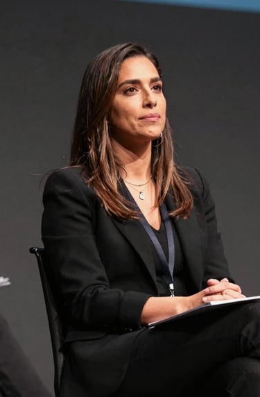 A powerful perspective shot of a professional Mexican woman leading a cybersecurity panel at a digital rights summit, looking confident under warm theater lighting, set against a simple and minimalist dark grey backdrop.