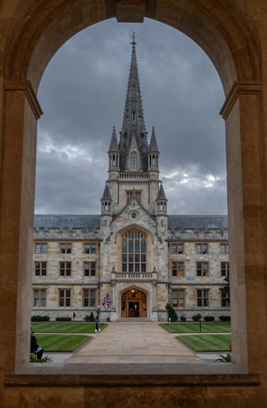 A view of a traditional university courtyard at dusk through a heavy stone window frame. The sky is a muted charcoal, and the stone is a soft cream, evoking a sense of heritage and serious academic identity.