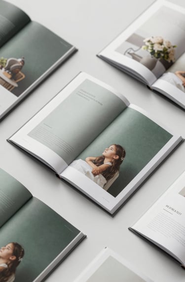 Top-down view of several open art catalogues showing high-quality photographic printing and elegant layout design. Soft morning light, sophisticated and clean. Palette: #293B37, #5B7B71, and #F1F4F2.