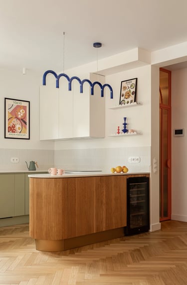 Szałwiowa kuchnia z wyspą i lamelami. Jadalnia z dębowym stołem i czerwonymi krzesłami.