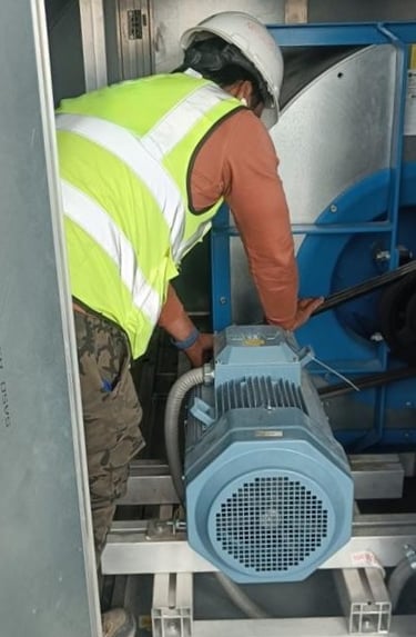 An HVAC technician performing maintenance on a large industrial air handling unit motor.