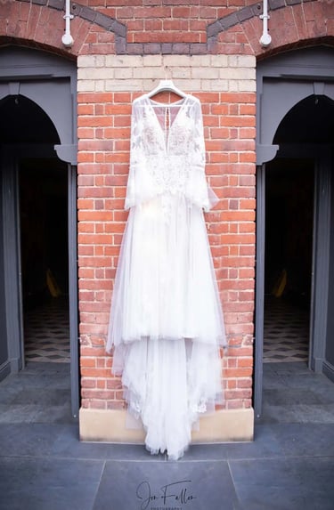 Elegant long-sleeved lace wedding dress hanging on a red brick wall between two arched doorways.