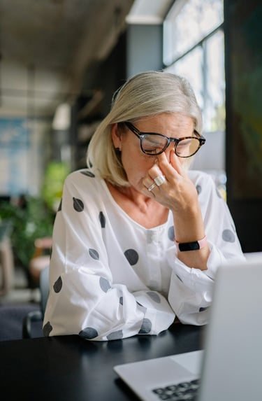 Anxious woman sits at her computer rubbing her eyes with tension