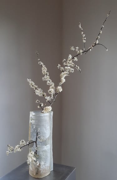 an icy glass vase with a flowering branche in it.