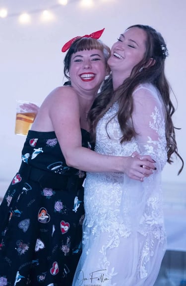 Smiling bride in lace wedding dress dancing and hugging a friend in a vintage rockabilly dress.