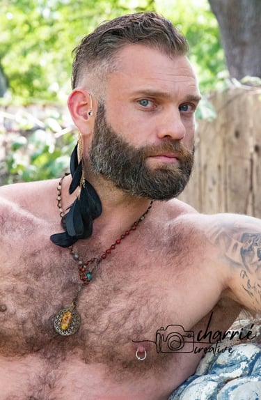 outdoor portrait of shirtless masseuse with a trimmed beard and hairy chest looking intrigued