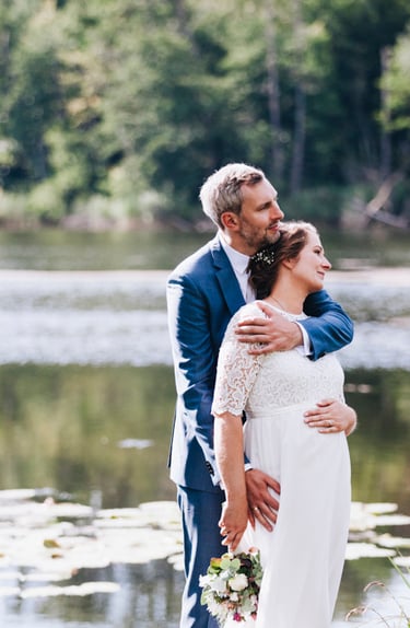 Braut und Bräutigam blicken neben einem See in die Ferne.