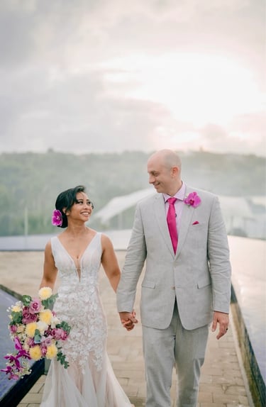 A smiling bride and groom holding hands while walking outdoors during a tropical destination wedding.