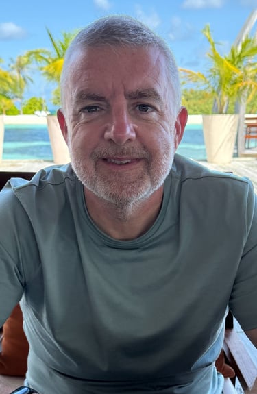 "Person seated at outdoor table in tropical resort with palm trees and lounge chairs nearby
