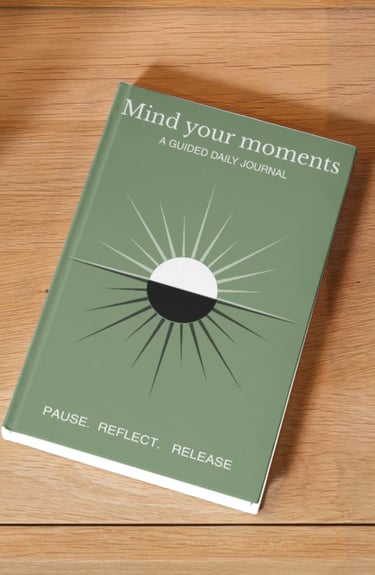 A sage green Mind Your Moments guided daily journal for mindfulness and reflection on a wooden surface.