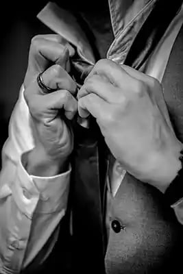 A groom in a formal waistcoat and dress shirt adjusts his necktie for a wedding ceremony.