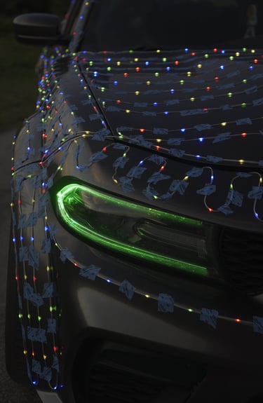 Black Dodge Charger hood covered in colorful Christmas LED lights with glowing green headlights.