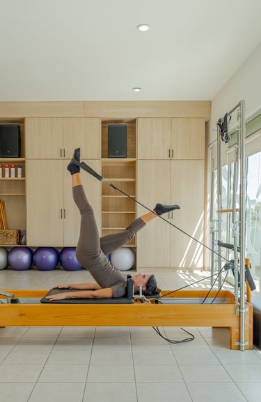 Woman lying on a Pilates Reformer doing a leg exercise using the foot straps in the Cabo San Lucas studio.