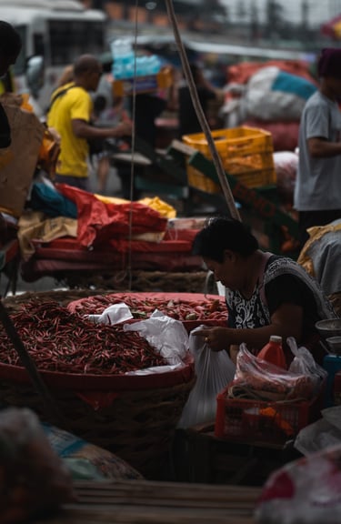 a woman is sitting at a market with many baskets of chili peppers