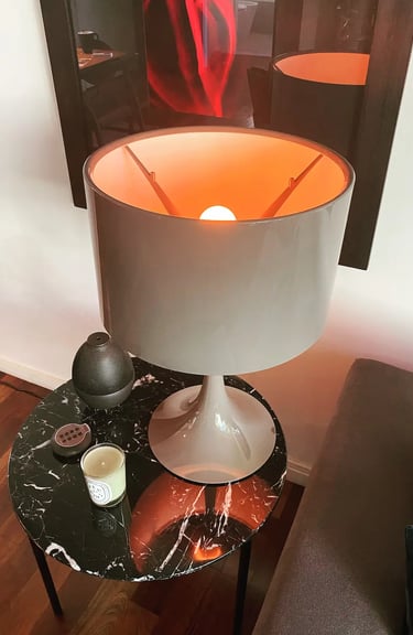 Mesa redonda de soporte para sillón con lámpara de diseño sobre su superficie estilo mármol y cuadro