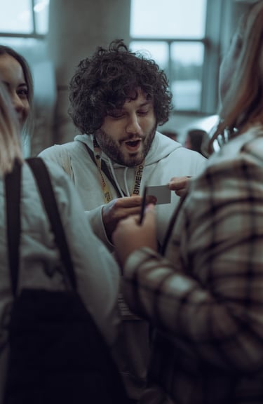 Man with curly hair wearing a BIME Pro lanyard exchanging business cards with two other attendees at BIME Bilbao. Networking 