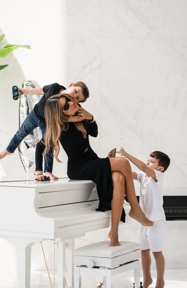 Mother in black dress playing with her two sons on a white piano.