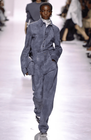 Bottega Veneta Spring/Summer 2026 Slate blue suede jumpsuit with woven clutch. 