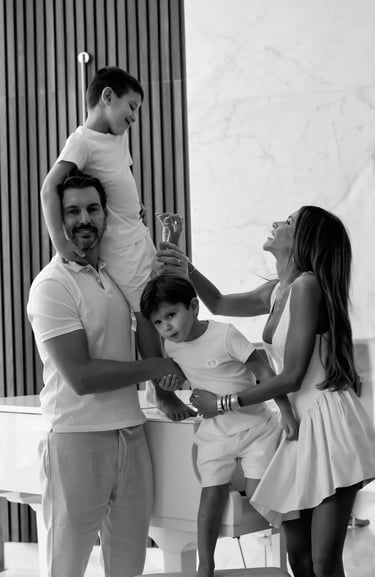 Black-and-white family photo of two parents playing with their sons indoors.