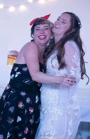 Smiling bride in lace wedding dress dancing and hugging a friend in a vintage rockabilly dress.