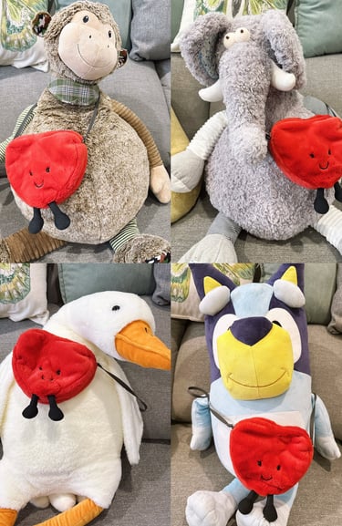 Four plush stuffed animals wearing a red heart-shaped crossbody bag with a smiley face.