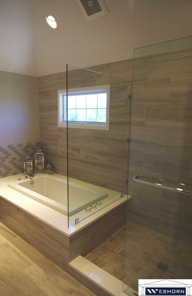 Modern master bathroom featuring a soaking tub next to a glass walk-in shower with neutral stone tile.
